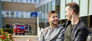 Twee mannen zitten op een bankje voor de entree van het Diakonessenhuis